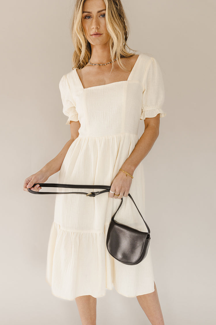 cream square neck dress with black handbag