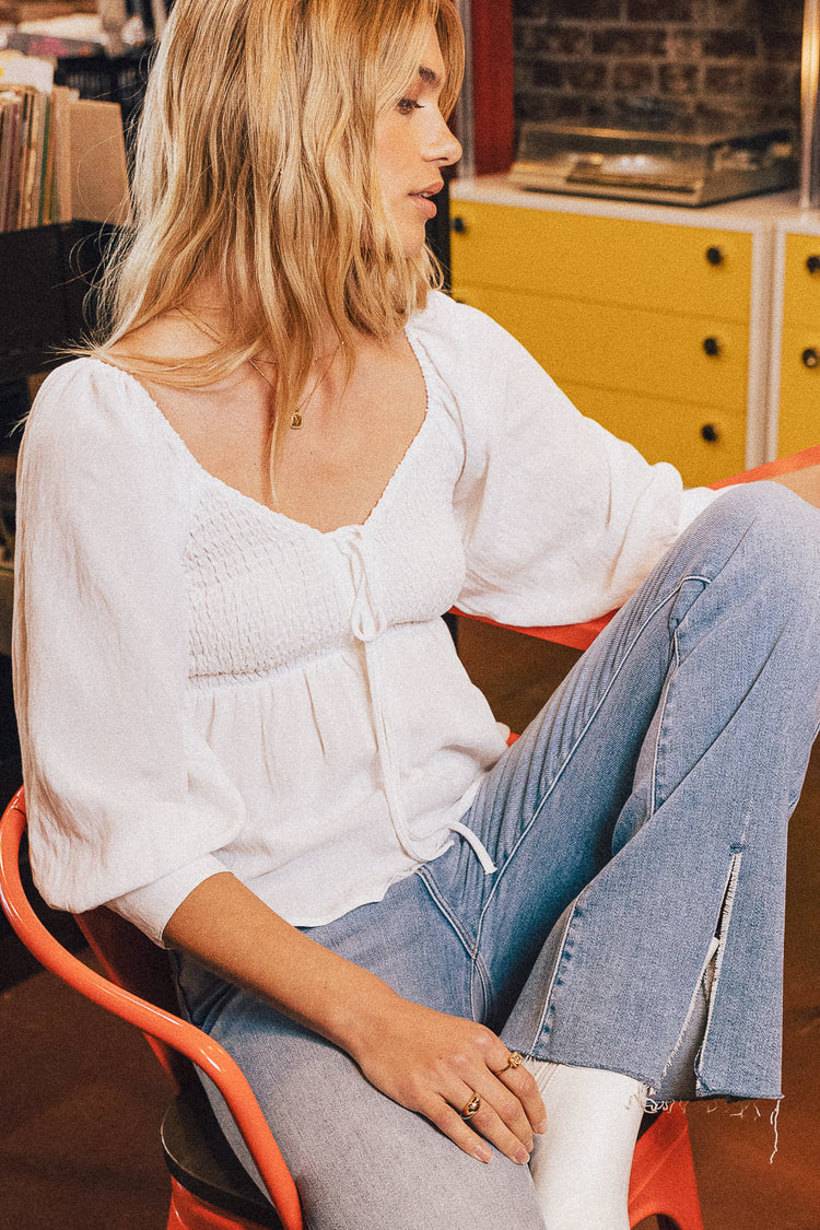 model sitting wearing a long sleeve smocked top and denim jeans