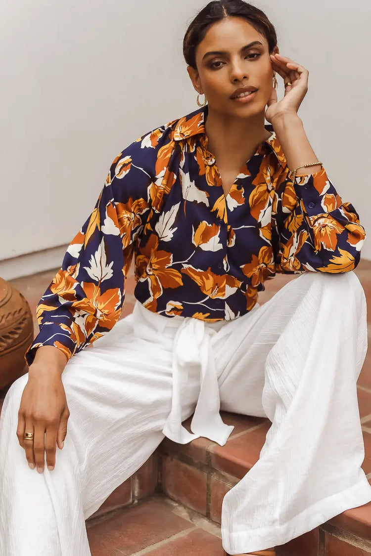 model sitting wearing a floral blouse and white pants