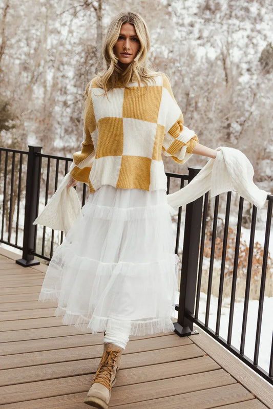 Checkered sweater in mustard paired with a white dress 