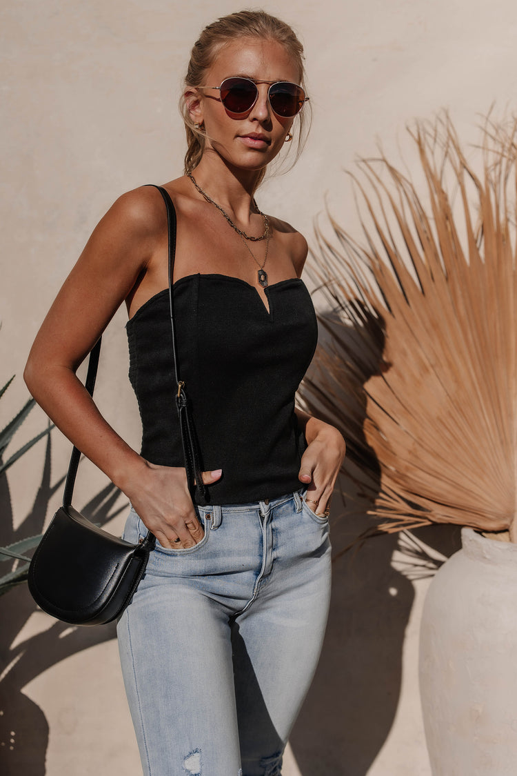 Model wears the Theresa Top in Black with light wash jeans and a black bag. Top is sleeveless with sweetheart neckline and smocked back.