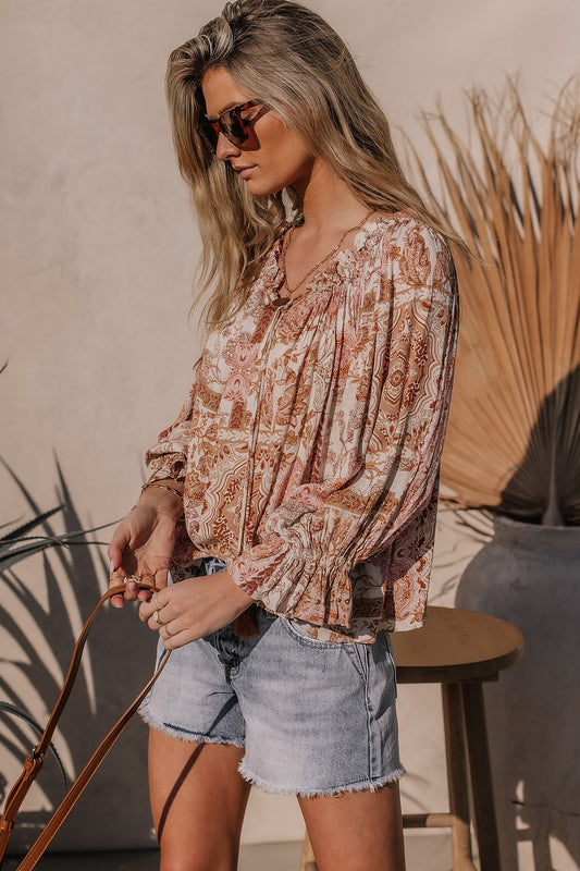 Model wears the Elianna Floral Top with light wash cutoff shorts and brown sunglasses. Top has relaxed fit, elastic cuffs, and tie neck detail.