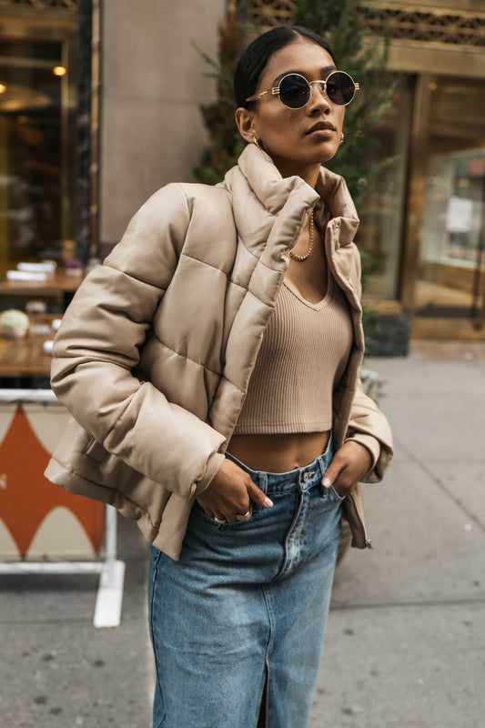 Model wears the Zaylee Vegan Leather Puffer Coat in taupe with a nude knit tank top and medium wash denim midi skirt.