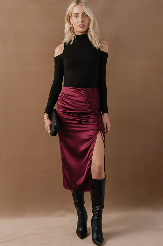 Model wears the Valerie Midi Skirt with knee high black boots and long sleeve black top. Skirt has ruching on the side and a long side slit.