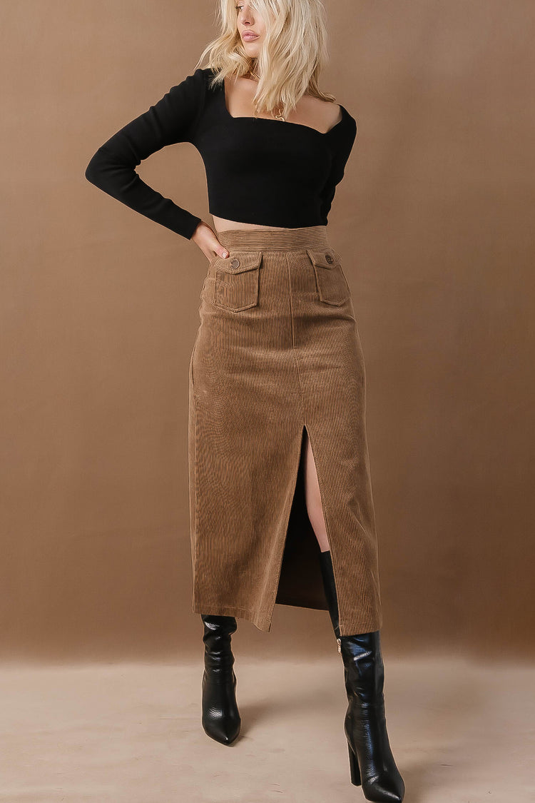 Model wears the Ninette Maxi Skirt in Mocha with a black long sleeve top and balck knee-high boots. Skirt is corduroy material and has front slit.