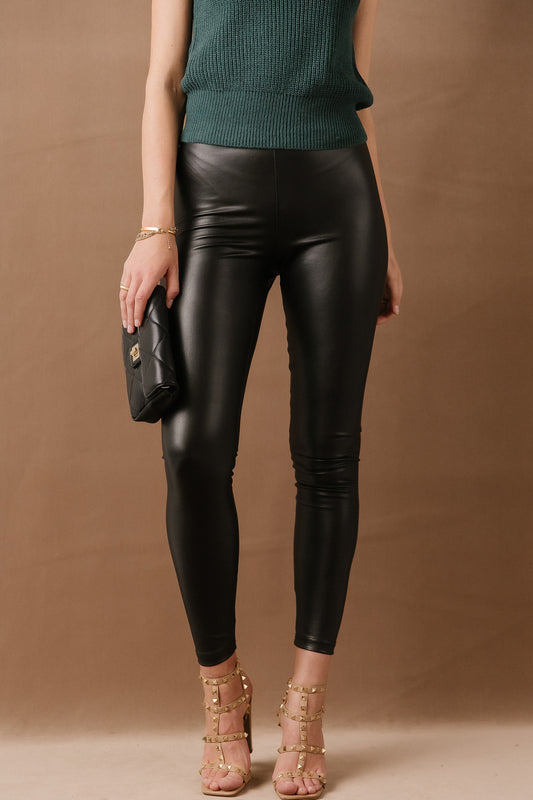 Model wears the Vero Moda Pepper Vegan Leather Pants with a green sweater vest, studded strappy heels, and a black clutch.