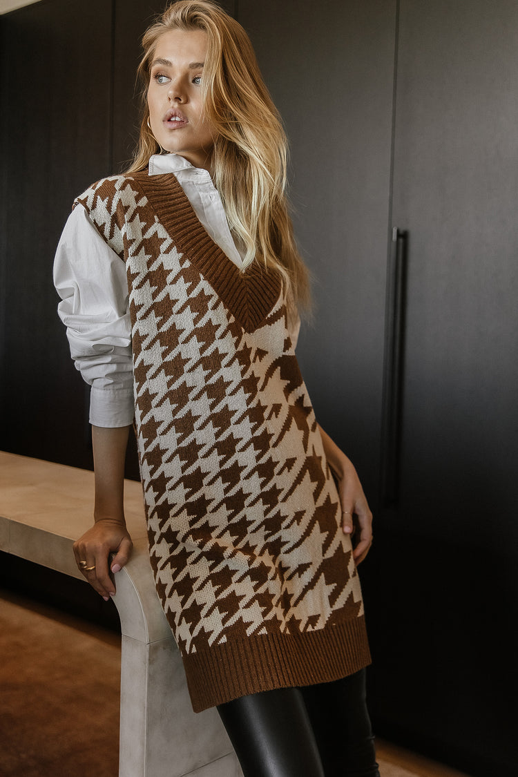 Model wears the Lillee Sweater vest in camel with black faux leather pants and a white button up shirt. Vest has a v-neck and houndstooth pattern.