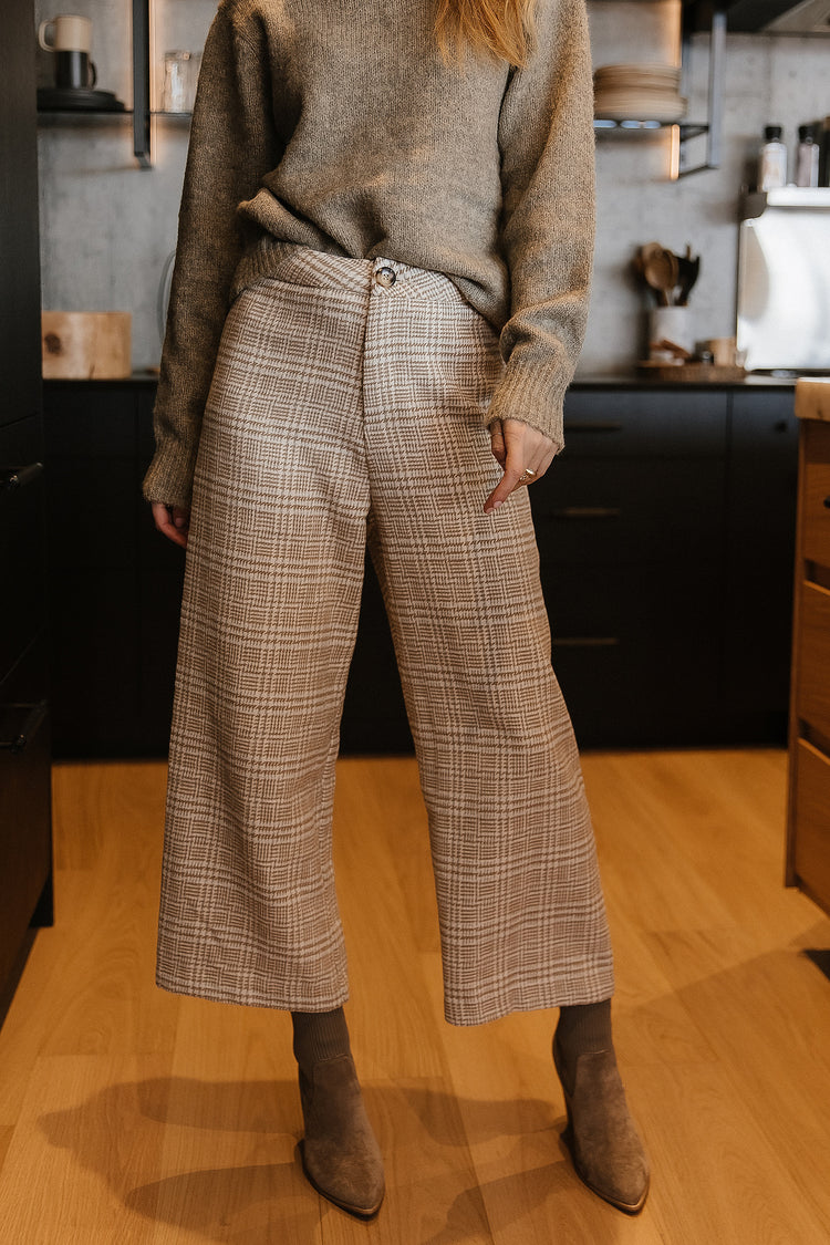 Model wears the Camryn Plaid Pants with a grey sweater and brown suede boots. Pants are wide leg and cropped and have a button closure.