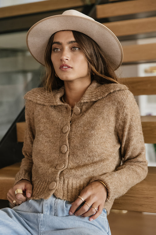 Model wears the Elora Cardigan Sweater with light wash denim and a taupe hat. Sweater has button front and wide collar.