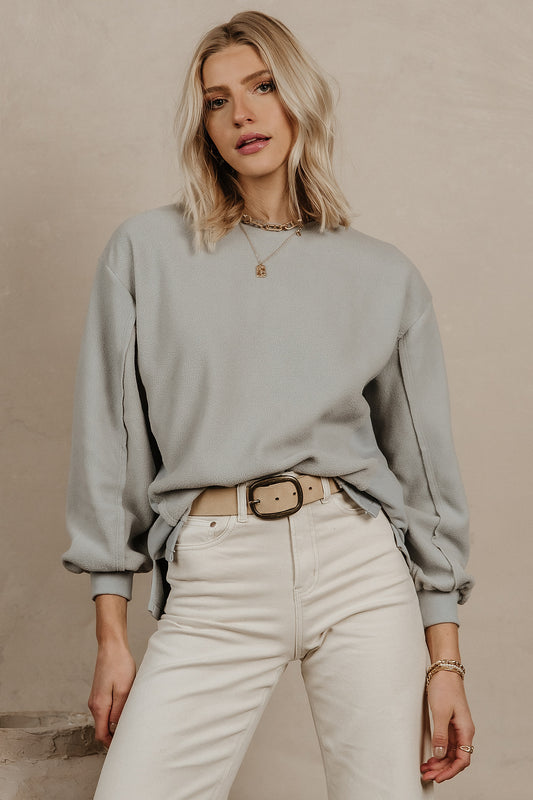 Model wears the Blythe Pullover in Blue with white denim with a taupe belt. Pullover has cinched sleeves and a relaxed fit. 
