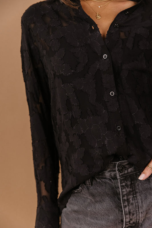 Model wears the Sloane Button Up in black with charcoal jeans. Top has lace material and is semi-sheer.