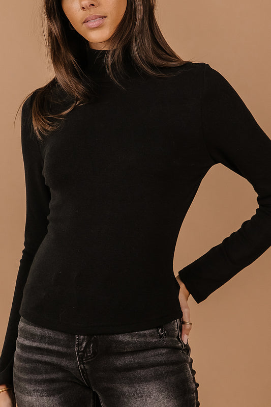 Model wears the DIann Mock Neck Top in Black with charcoal wash denim. Top is slim fitting on the body and has long sleeves.