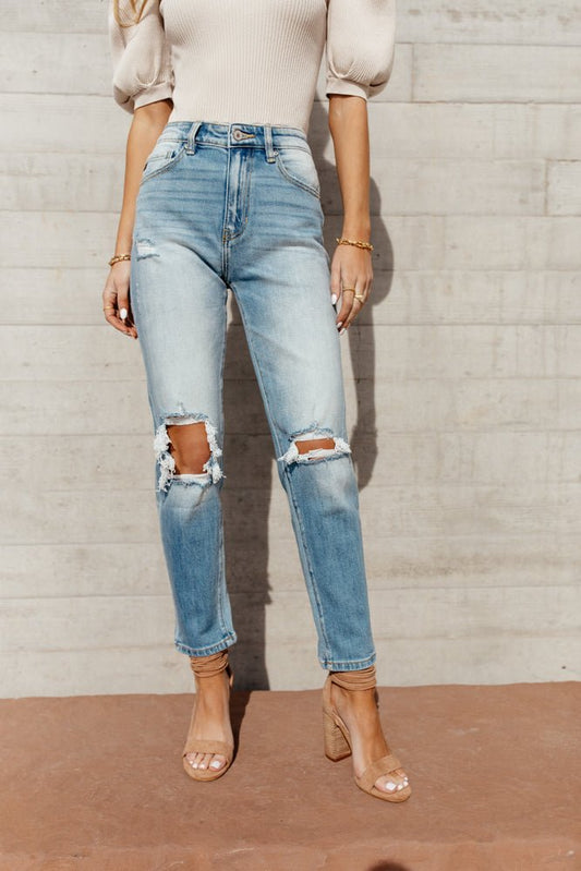 Model wears the KanCan Delila Mom Jeans with a cream bodysuit and nude heels. Jeans have rips in the knees and tapered ankles.