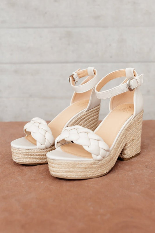 The Roccio Espadrilles are heeled and platformed shoes with a braided toe strap, thin ankle strap with a buckle, and faux leather material.
