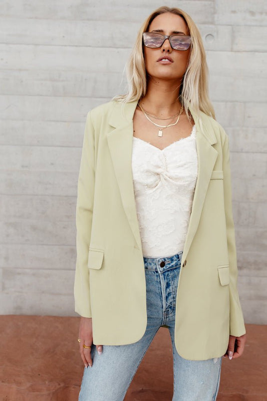 woman standing in light green blazer with sunglasses and jeans