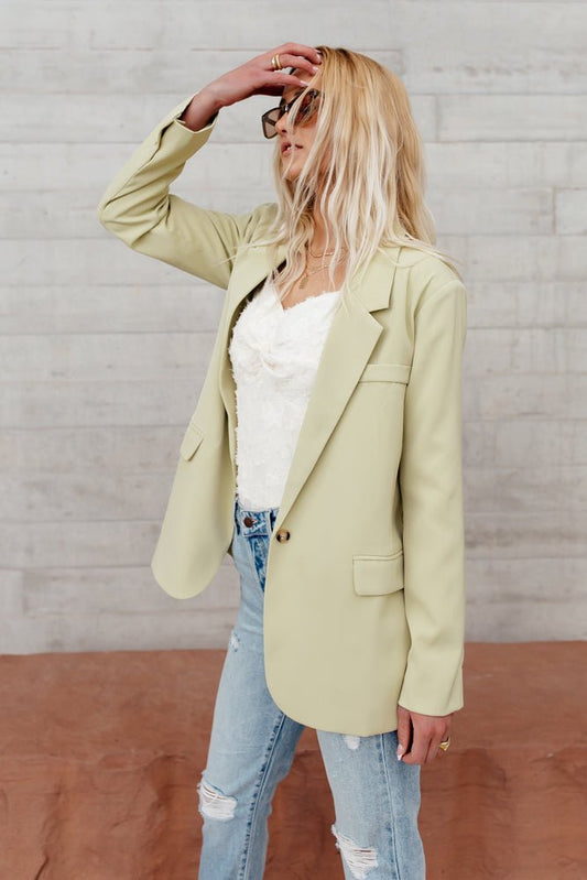 Model wears the Crystal Blazer in Lime with light wash jeans and a white top. Blazer has button closure, faux pockets, and slim fit.