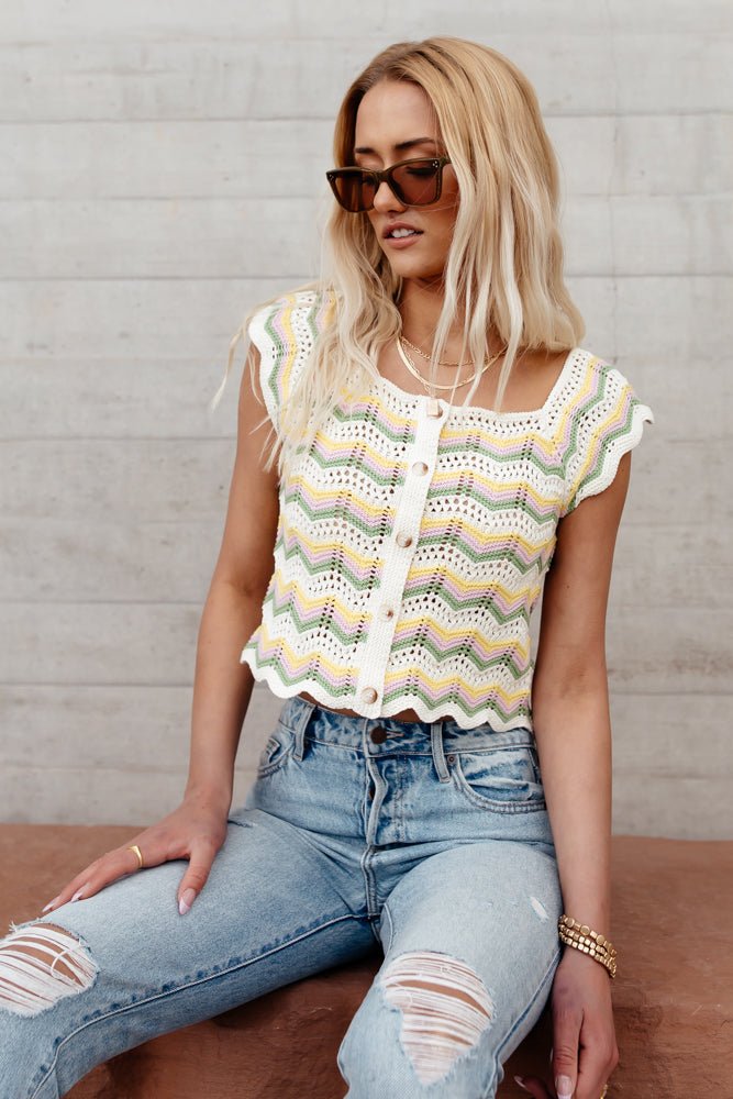 Model wears the Tonya Crochet Top with light wash jeans and brown sunglasses. Top has square neck, button front, and chevron knit pattern.