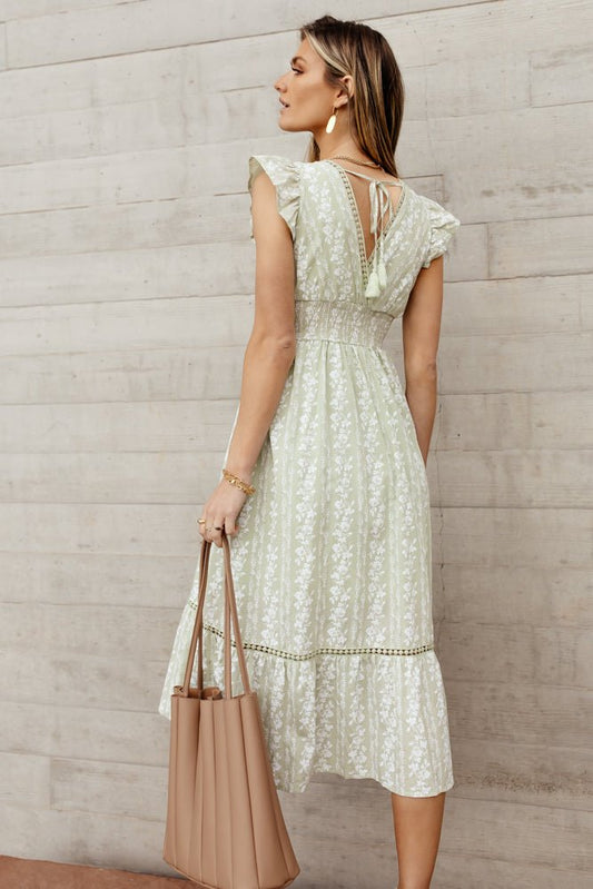 Model wears the Pippa Midi Dress with a nude purse and gold jewelry. Dress has flutter sleeves, tie back detail,  elastic waist, and floral pattern.