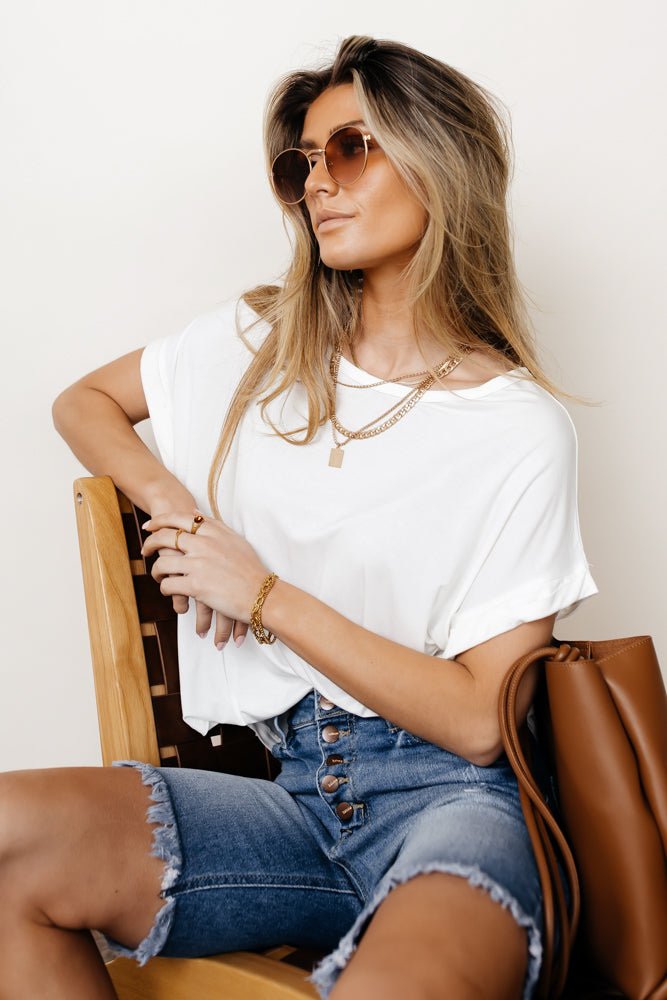 Model wears the Dempsey Rolled Sleeve Tee in White with medium wash bermudas and brown sunglasses. Tee has wide round neck and relaxed fit.
