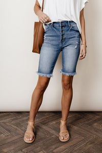 Model wears the Carmen Button Fly Bermuda in medium wash with a white top and tan sandals. Shorts have frayed hem and distressing.