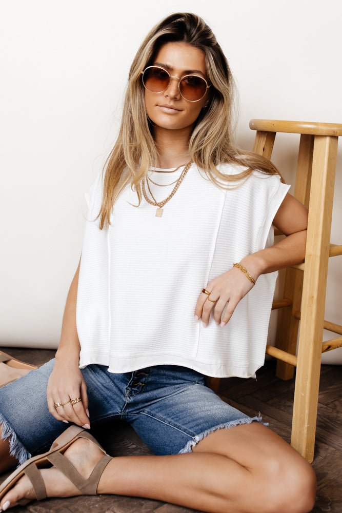 Model wears the Tilly Top in White with dark wash bermudas and taupe sandals. Top has cap sleeves, round neck, and oversized fit.