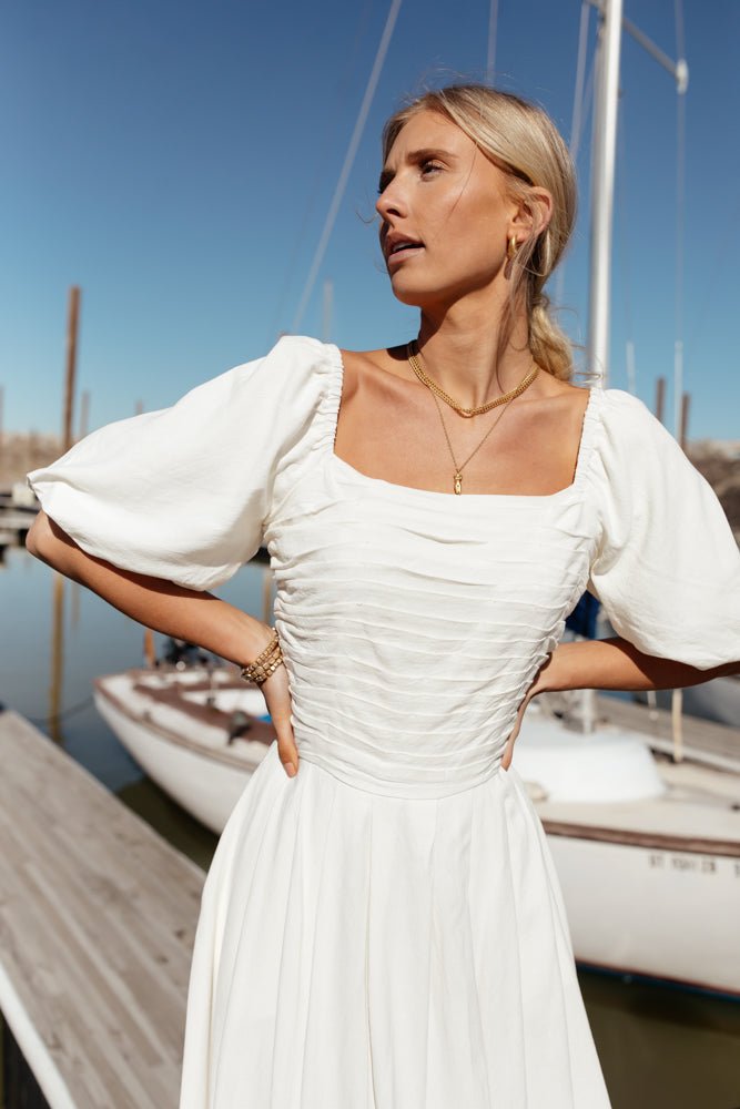 Model wears the Maika Midi Dress with gold jewelry. Dress has puff sleeves, square neck, and fold details on the bodice.