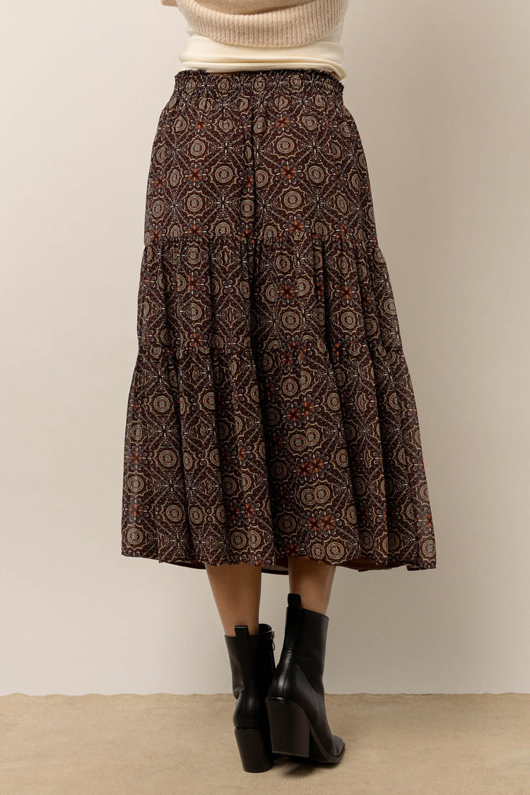 model is wearing a midi length printed skirt with black boots and cream sweater