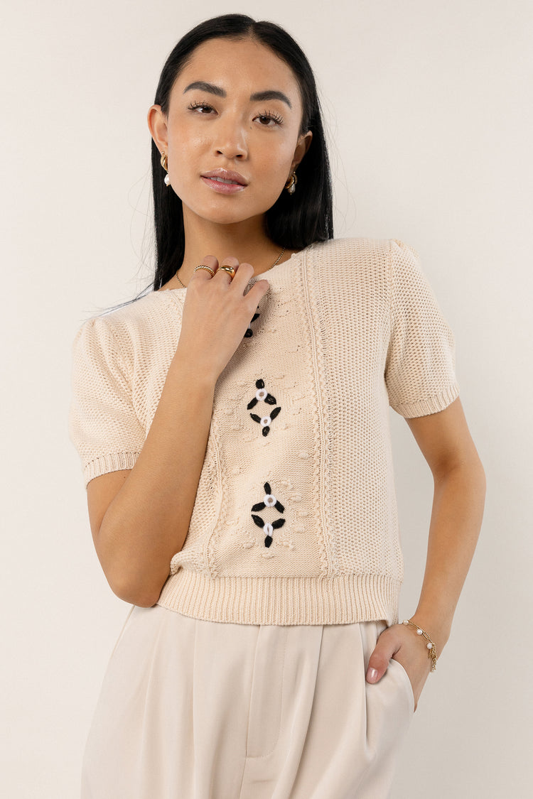model wearing short sleeve knit sweater with black flower detail