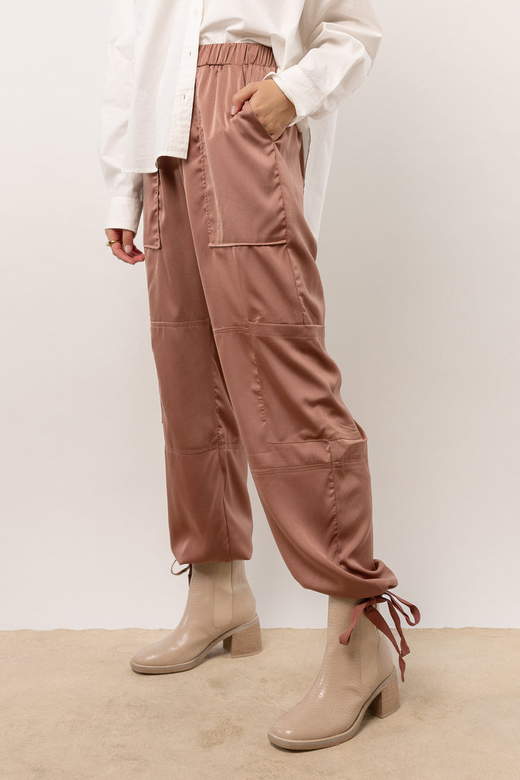 Model wearing rose satin cargo pants with elastic waist and ankle tie details