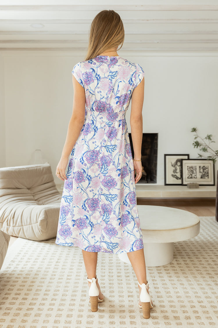 Backside of pink and blue floral printed midi dress with white heels and synched mid section