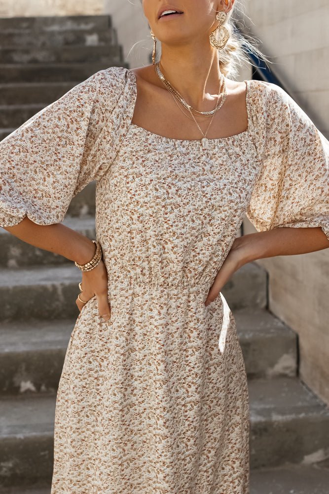 Model is wearing a floral midi dress with a square neckline, puff sleeves, and gold jewelry as accessories.
