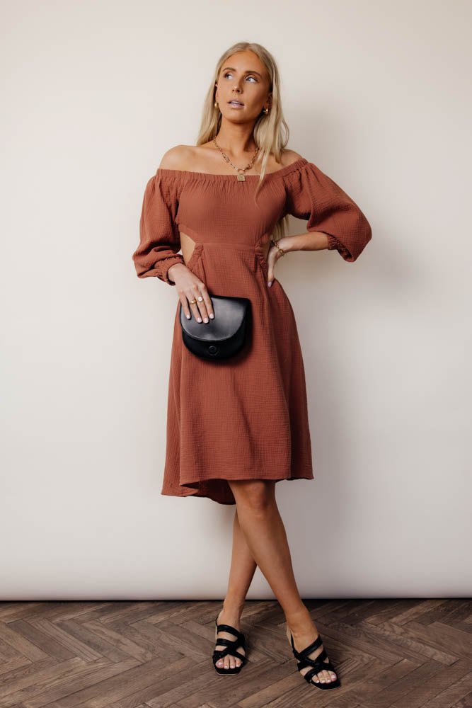 A model standing in front of a white background wearing a brown off the should midi dress