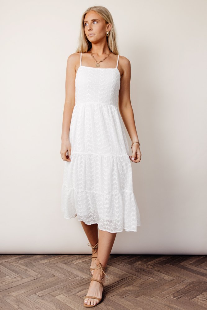 While wearing open-toed heels, this model poses in a tiered square tank midi dress in front of a white wall.