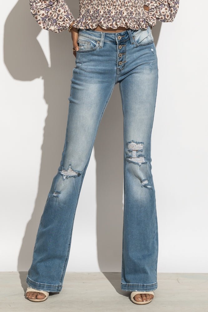 A woman with her hands on her hips modeling flared distressed jeans.