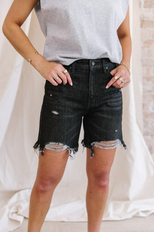a woman wearing a pair of high rise denim shorts in black 