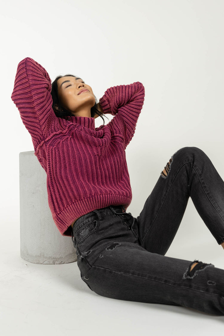 Model wearing magenta cable-knit sweater paired with black distressed denim