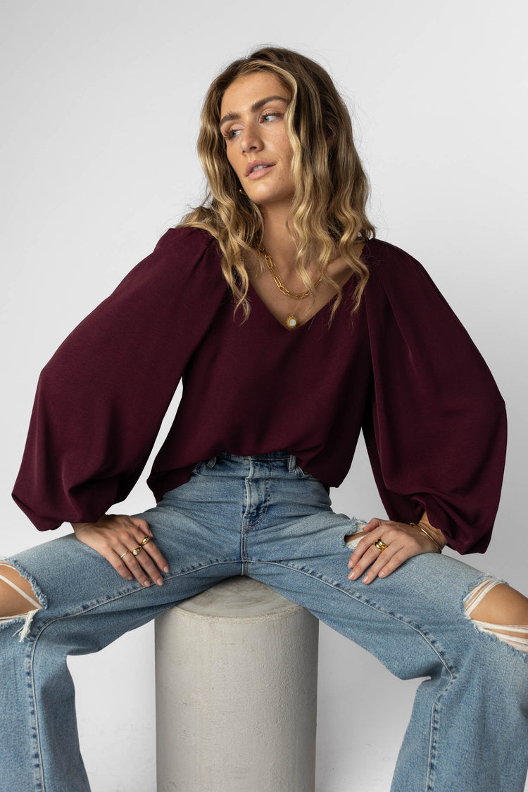 model wearing burgundy blouse with long balloon sleeves paired with distressed denim