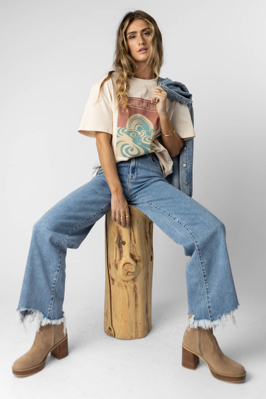model wearing cream graphic tee paired with light wash distressed denim and tan boots