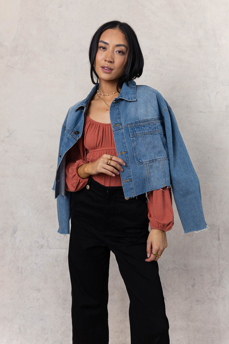 model wearing rust long sleeve bodysuit paired with cropped denim jacket and wide leg pants