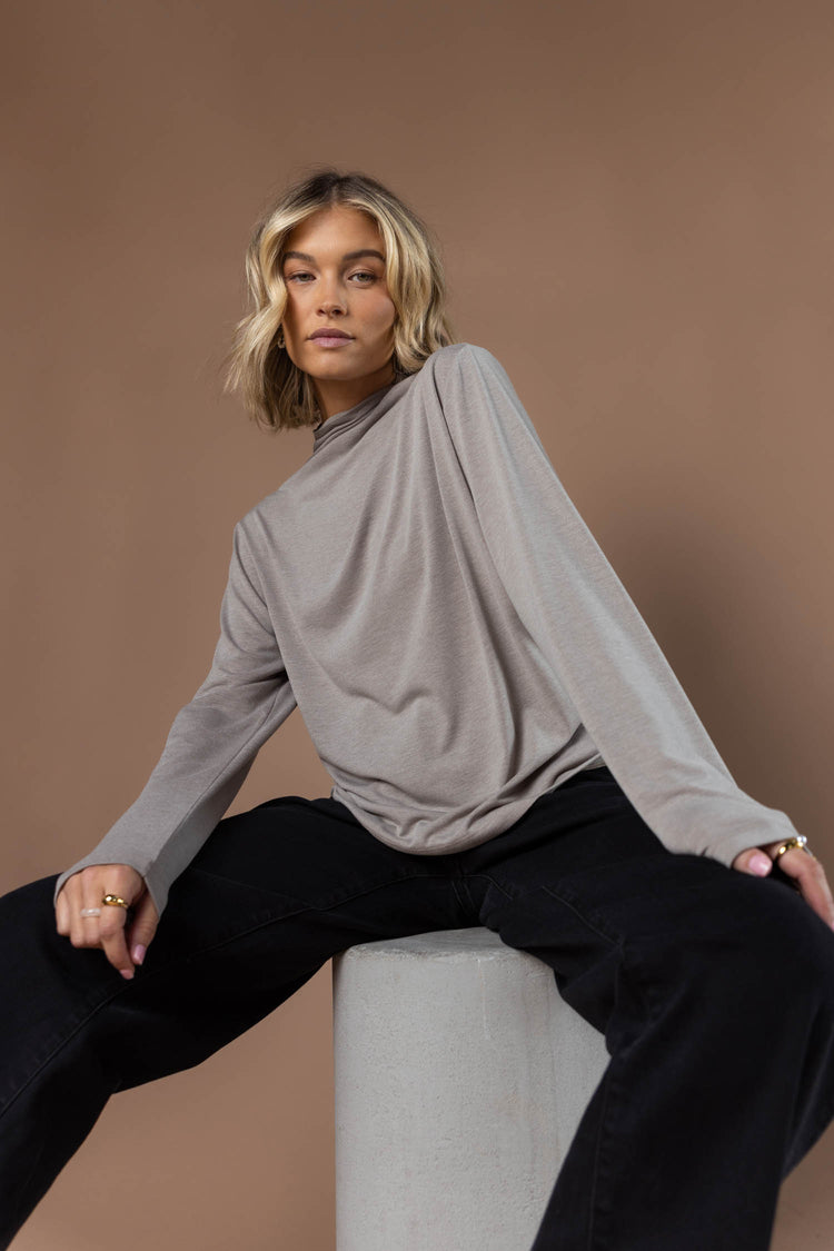 model wearing long sleeved taupe mock neck shirt paired with black wide leg pants