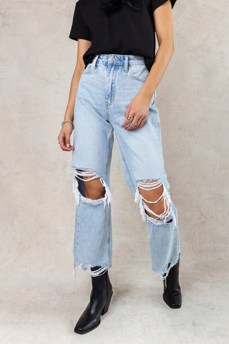 model wearing light wash wide leg distressed denim with holes in the knees paired with black boots