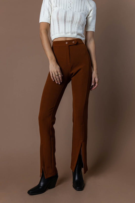 model wearing rust dress pants with front zipper and ankle paired with black boots and cream shirt