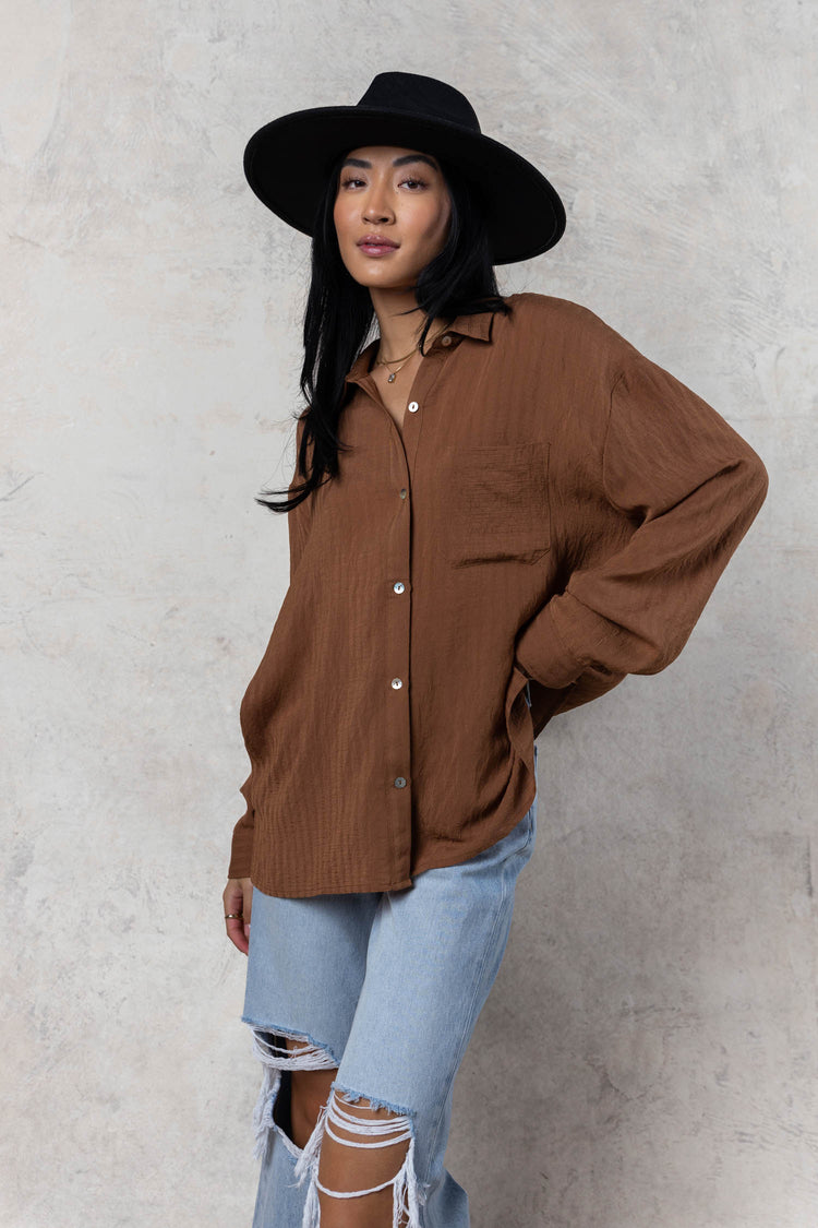 model wearing camel button down with black wide brimmed hat paired with light wash distressed jeans