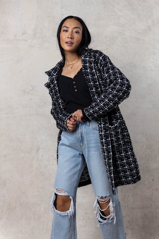 model wearing long black and white plaid collared open jacket paired with distressed denim and black long sleeve 