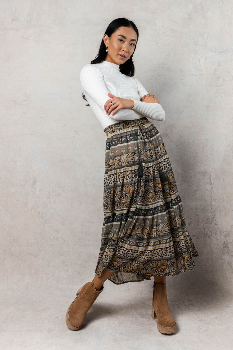 model is wearing printed skirt with brown boots and white turtleneck