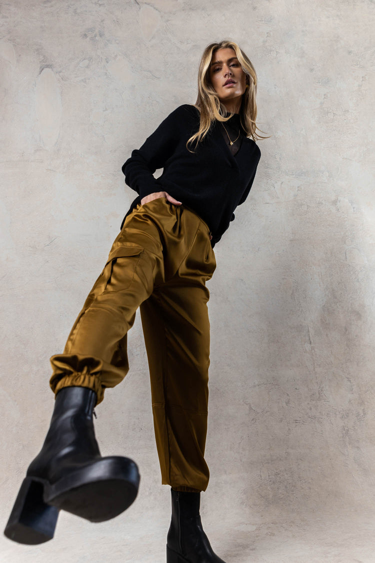 model wearing silky olive cargo pants with elastic cuff at the ankle paired with black boots