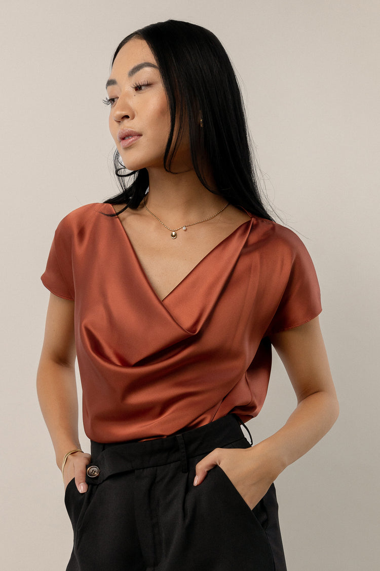 model wearing rust short sleeve satin blouse with cowlneck 